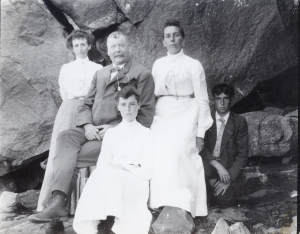 Mattie Nichols Eames Standing to the right of a seated Ed Nelson Eames with a kneeling Harold Eames with an unknown women between the two men and an unknown women seated in front of Ed. Big Rocks behidn them all.